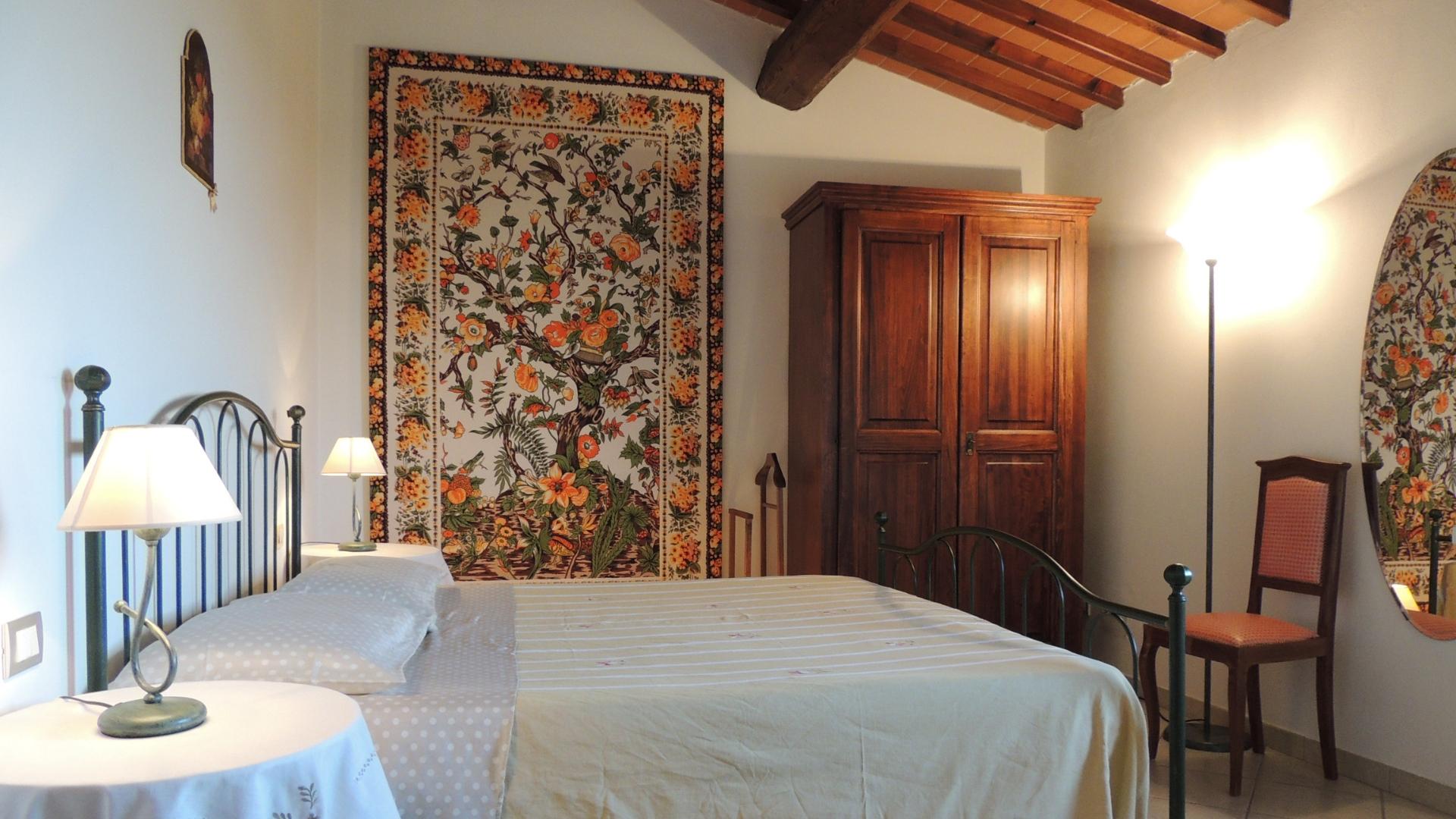 Camera da letto accogliente con arazzo floreale, mobili in legno e illuminazione soffusa.