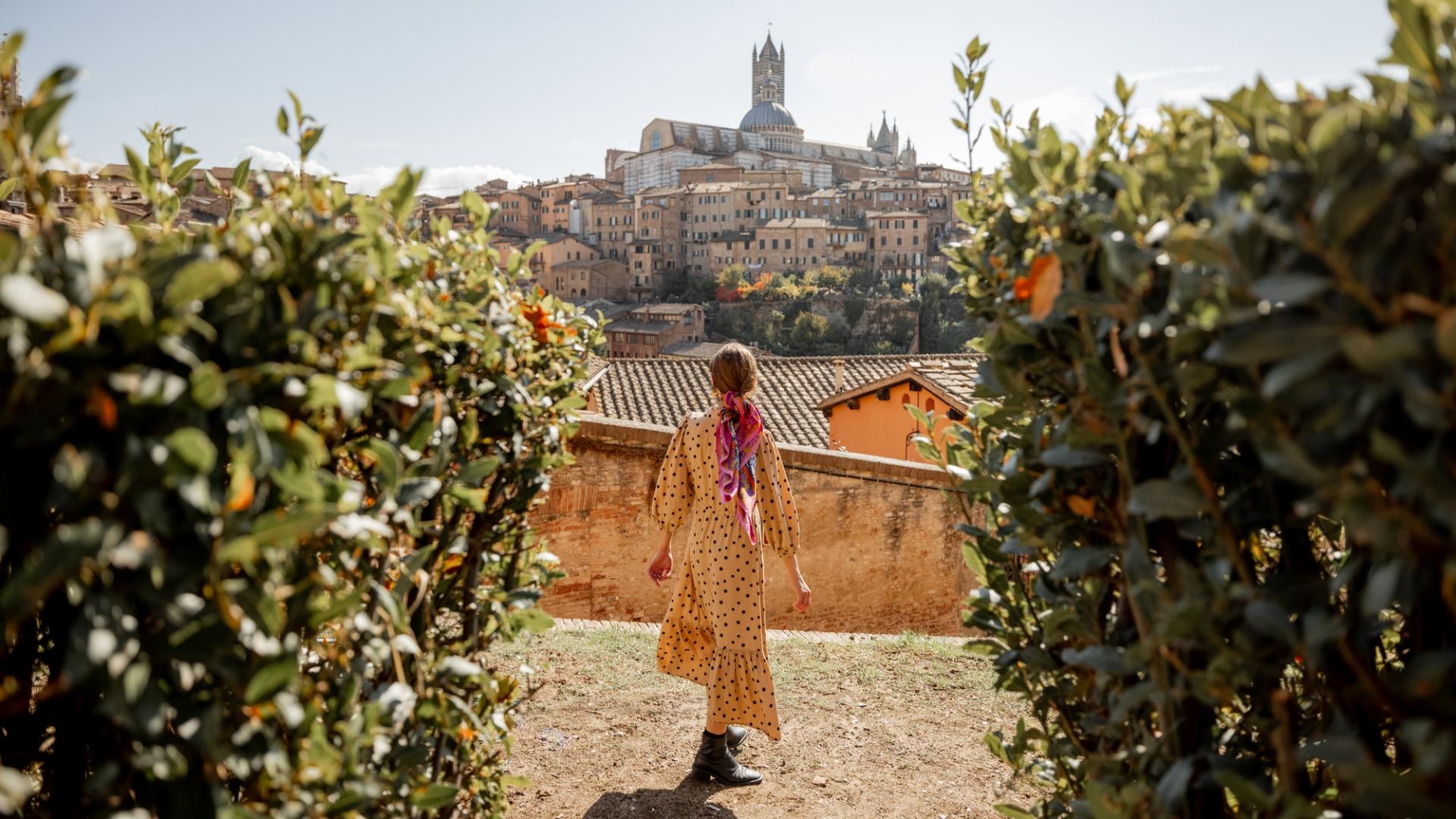 Donna con abito a pois osserva la città di Siena tra le siepi.
