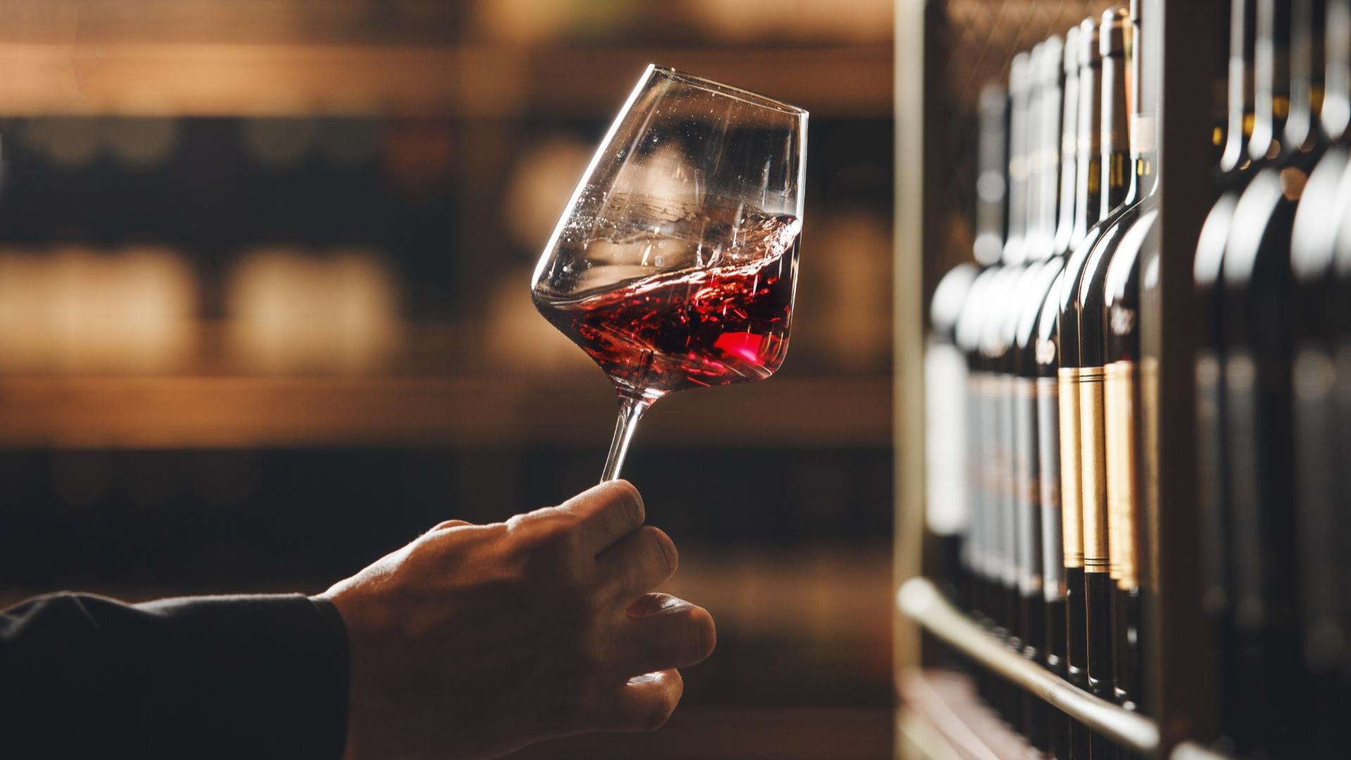 Calice di vino rosso in una cantina, circondato da bottiglie sugli scaffali.