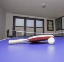 Racchetta e pallina su un tavolo da ping pong in una stanza chiusa.