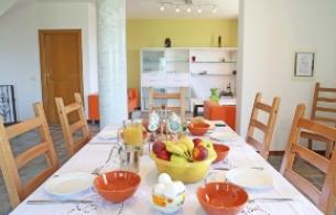 Tavola apparecchiata con frutta, uova e bevande in una sala da pranzo luminosa.