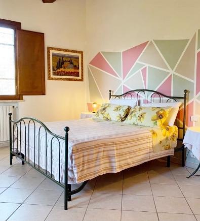 Camera da letto con letto in ferro e parete geometrica colorata, luminosa e accogliente.