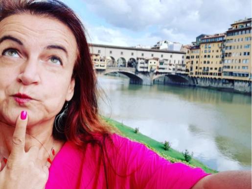Donna pensierosa davanti al Ponte Vecchio a Firenze, indossa una maglia rosa brillante.