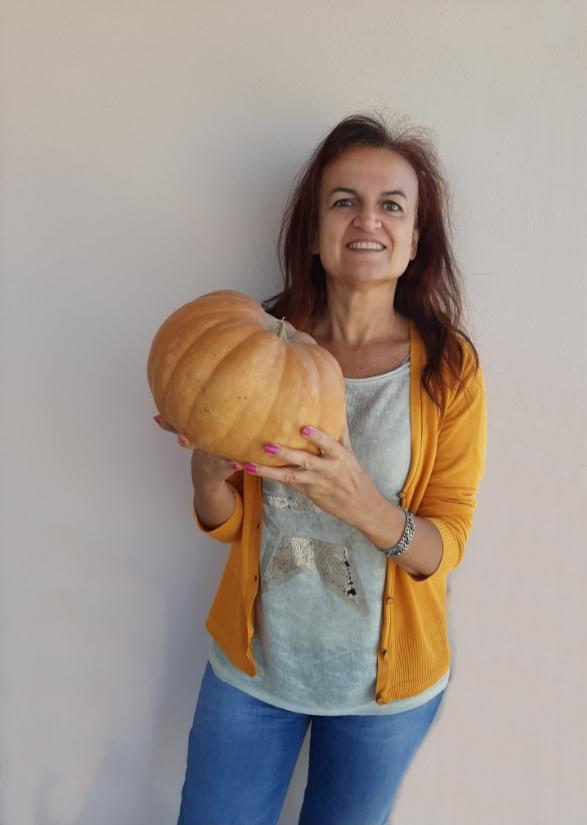 Donna sorridente con cardigan giallo tiene una grande zucca.