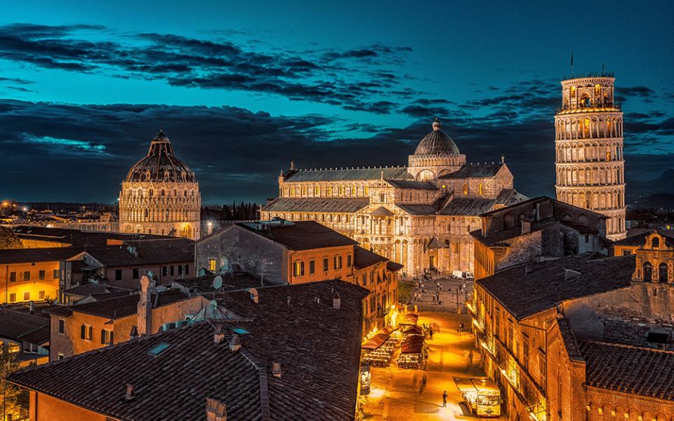 Vista notturna della Piazza dei Miracoli con la Torre di Pisa illuminata.