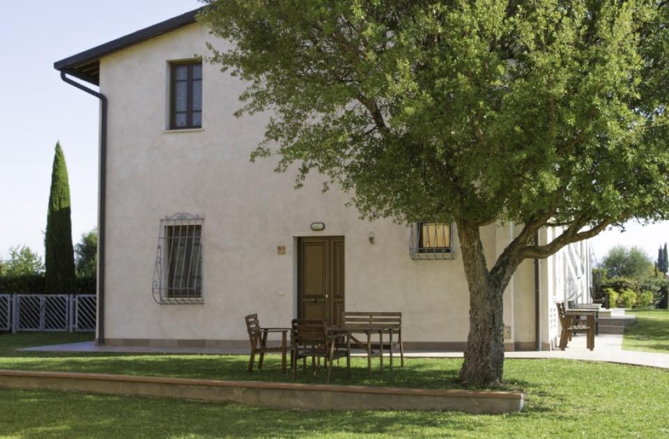 Casa con giardino, tavolo all'aperto sotto un albero, giornata soleggiata.