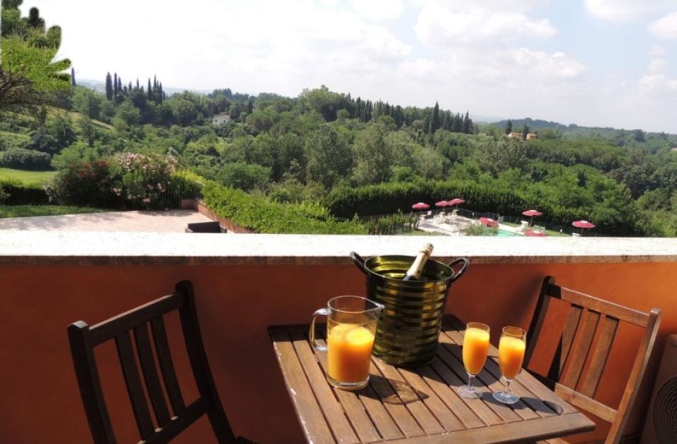 Terrazza con vista campagna, tavolo con succo d'arancia e bottiglia in secchiello.