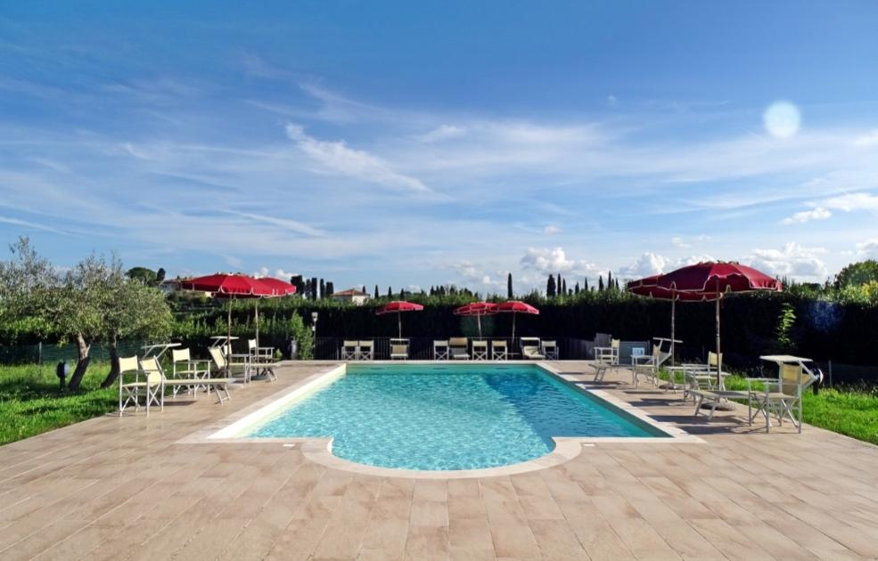 Piscina all'aperto con sedie, ombrelloni rossi e cielo sereno.