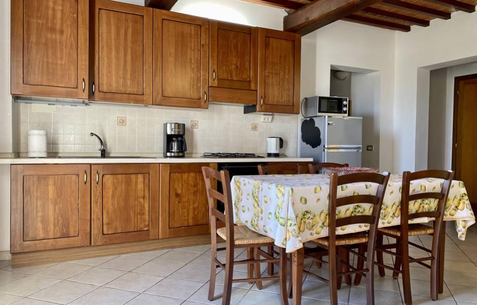Cucina rustica con mobili in legno, tavolo con tovaglia decorata e elettrodomestici moderni.