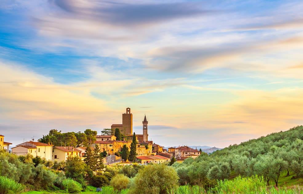 Suggestivo borgo toscano al tramonto, circondato da colline e uliveti.
