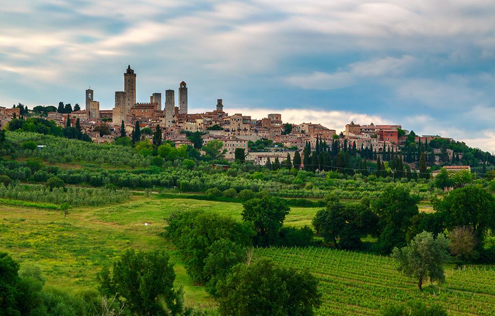 Panorama collinare con chiesa storica e paesaggio verdeggiante, illuminato dalla luce del tramonto.