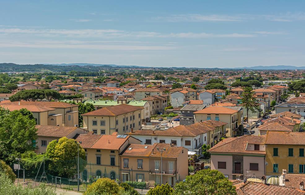Vista panoramica di una città con tetti rossi e paesaggio collinare sullo sfondo.