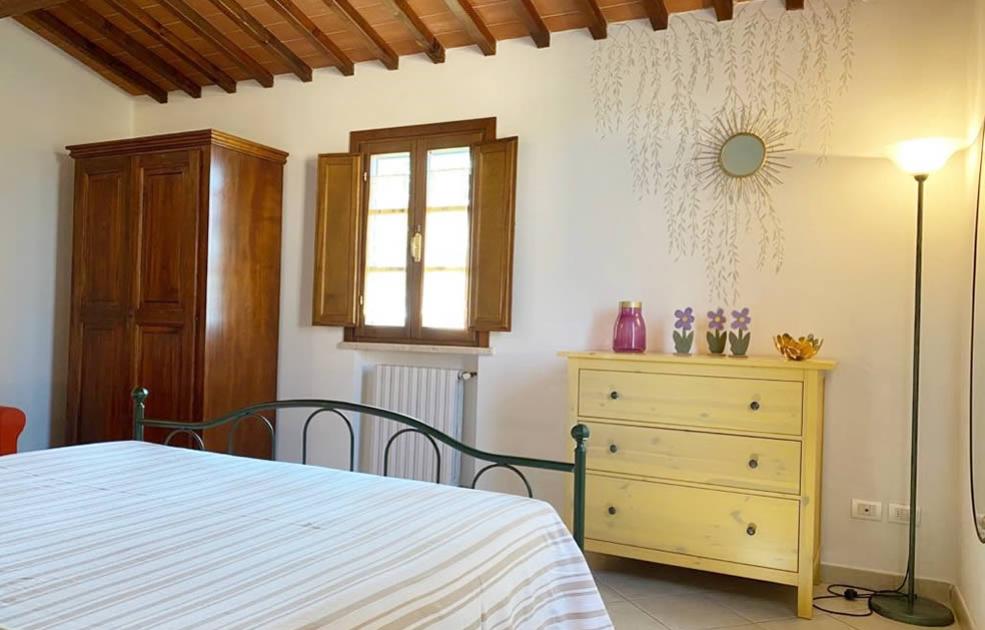 Camera accogliente con letto, armadio in legno, cassettiera gialla e decorazioni floreali.