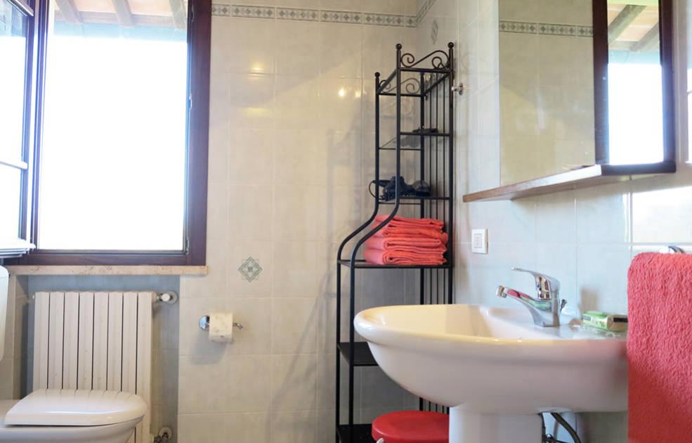 Bagno luminoso con lavabo, scaffale, asciugamani rossi e finestra grande.