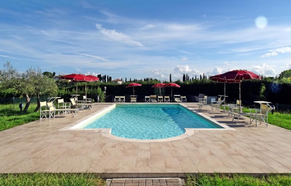 Piscina all'aperto con ombrelloni rossi e sedie, circondata da verde.