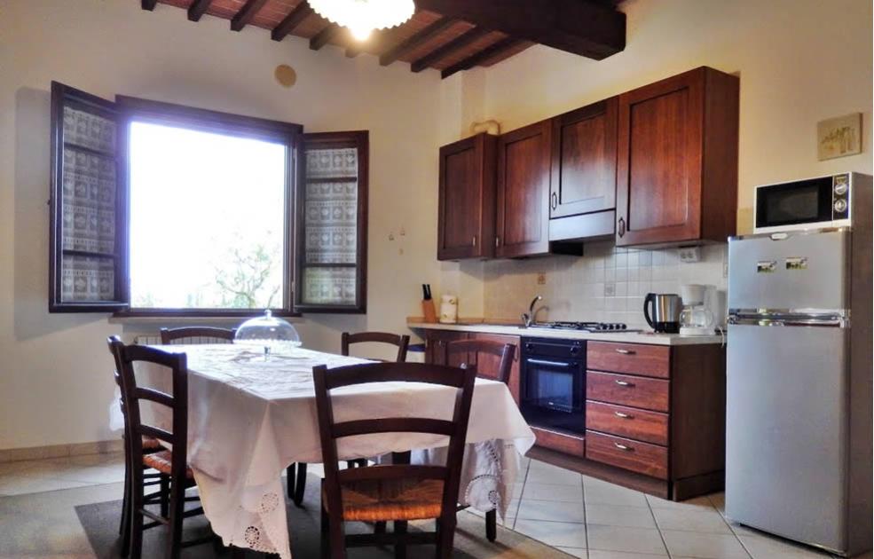 Cucina accogliente con tavolo apparecchiato, mobili in legno e finestre luminose.