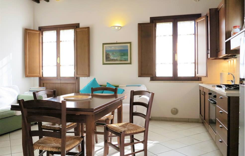 Soggiorno luminoso con cucina, tavolo in legno e divano, arredato in stile classico.