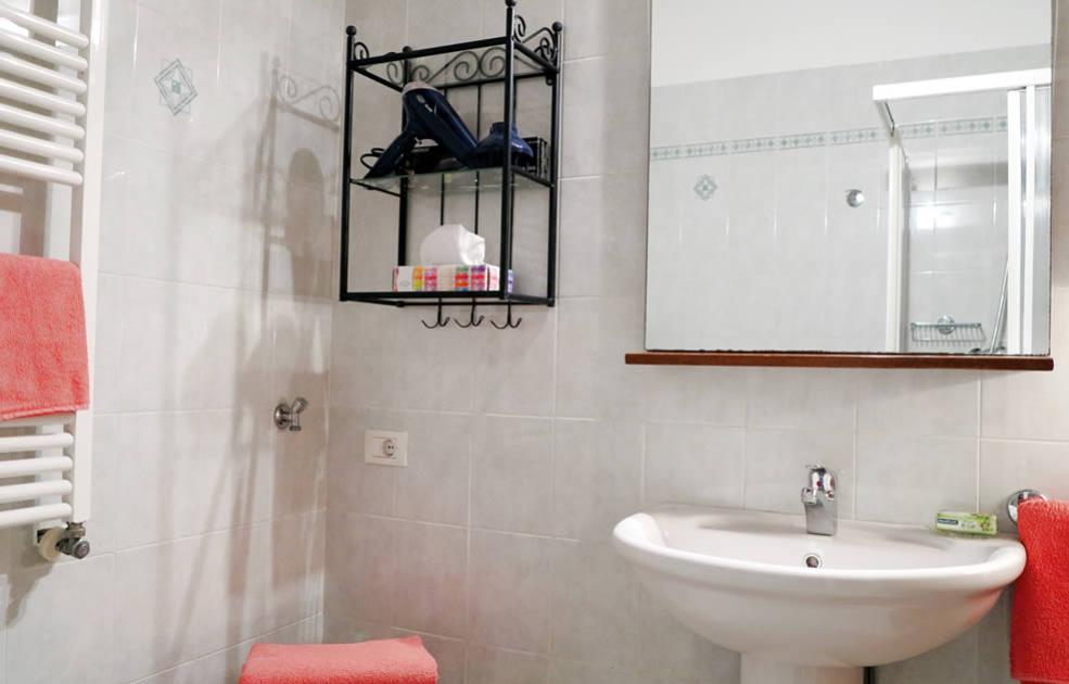Bagno con lavabo, specchio, scaffale e asciugamani rosa su piastrelle bianche.